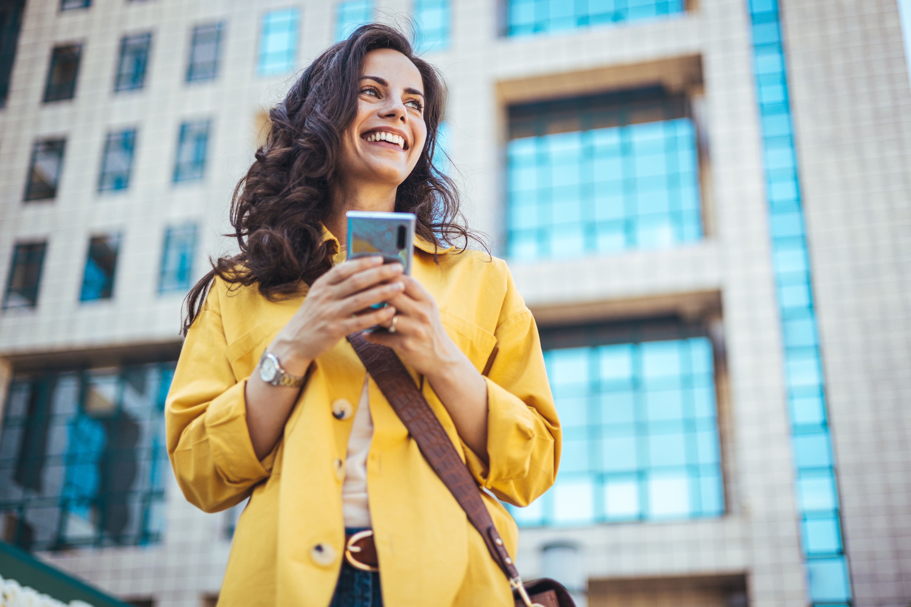 A smiling resident holding a smartphone outdoors and walking the downtown neighborhood near Avian Apartments in Colorado Springs, CO.