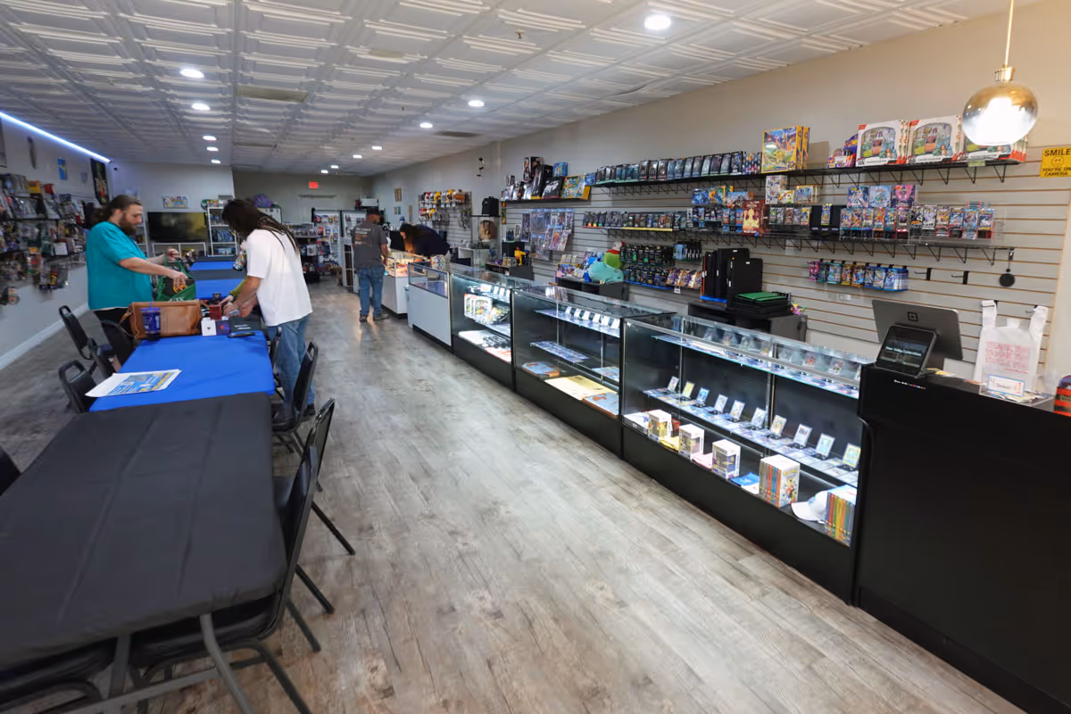 A picture of the inside of a game store, featuring long gaming tables and glass display cases.