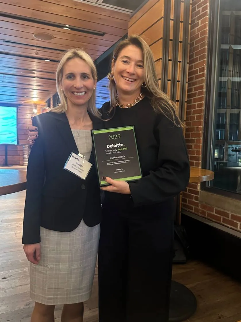 Two women smiling indoors, one wearing a business suit and a badge, the other holding a Deloitte Technology Fast 500 North America 2025 award plaque.