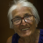 An elderly gray-haired woman with glasses smiles