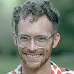 A young man with glasses smiles at the camera