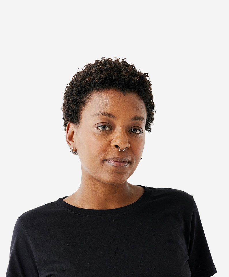 A woman with short curly hair and a nose piercing smiles at the camera.