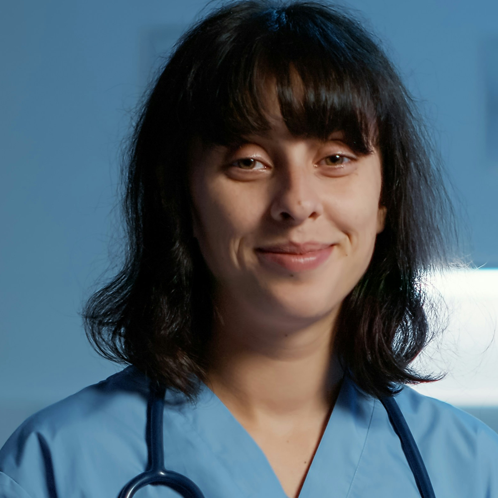 Portrait of female medical professional with shoulder-length dark hair wearing blue scrubs