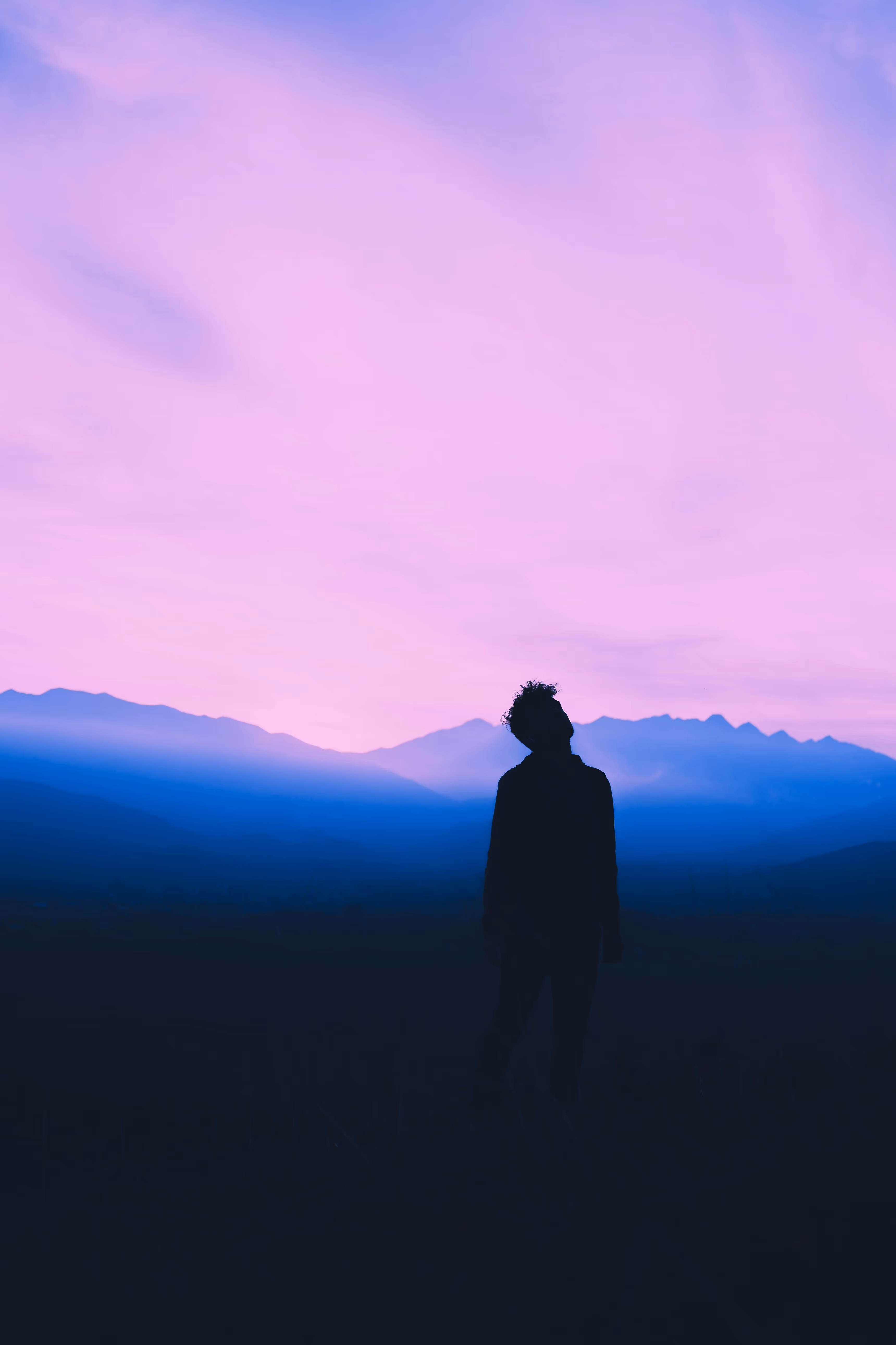 Silhouette of a person standing against a pink and blue mountain sunset.