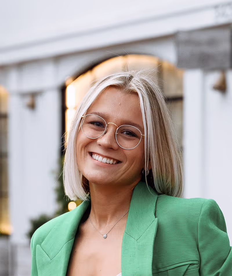 Daria Smith — young woman with blonde bob haircut and glasses, smiling in a green blazer.