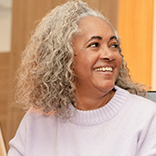 Smiling older woman with gray curly hair in lavender sweater.