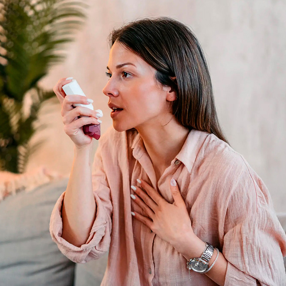 Woman using an inhaler during a shortness of breath episode at home.
