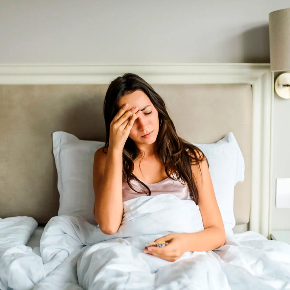 Unwell woman in bed with thermometer, showing signs of temperature sensitivity.