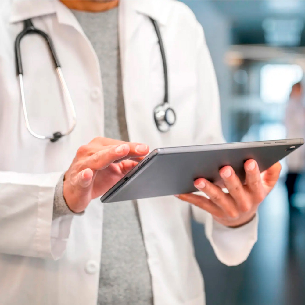 A doctor in a white coat with a tablet and a stethoscope, working in a medical facility.