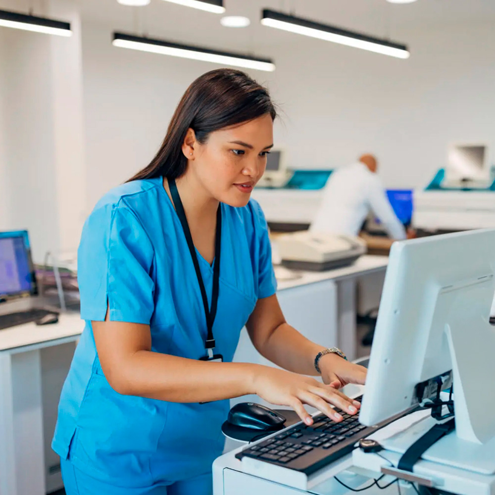 Healthcare professional in blue scrubs working on a computer at a medical facility.
