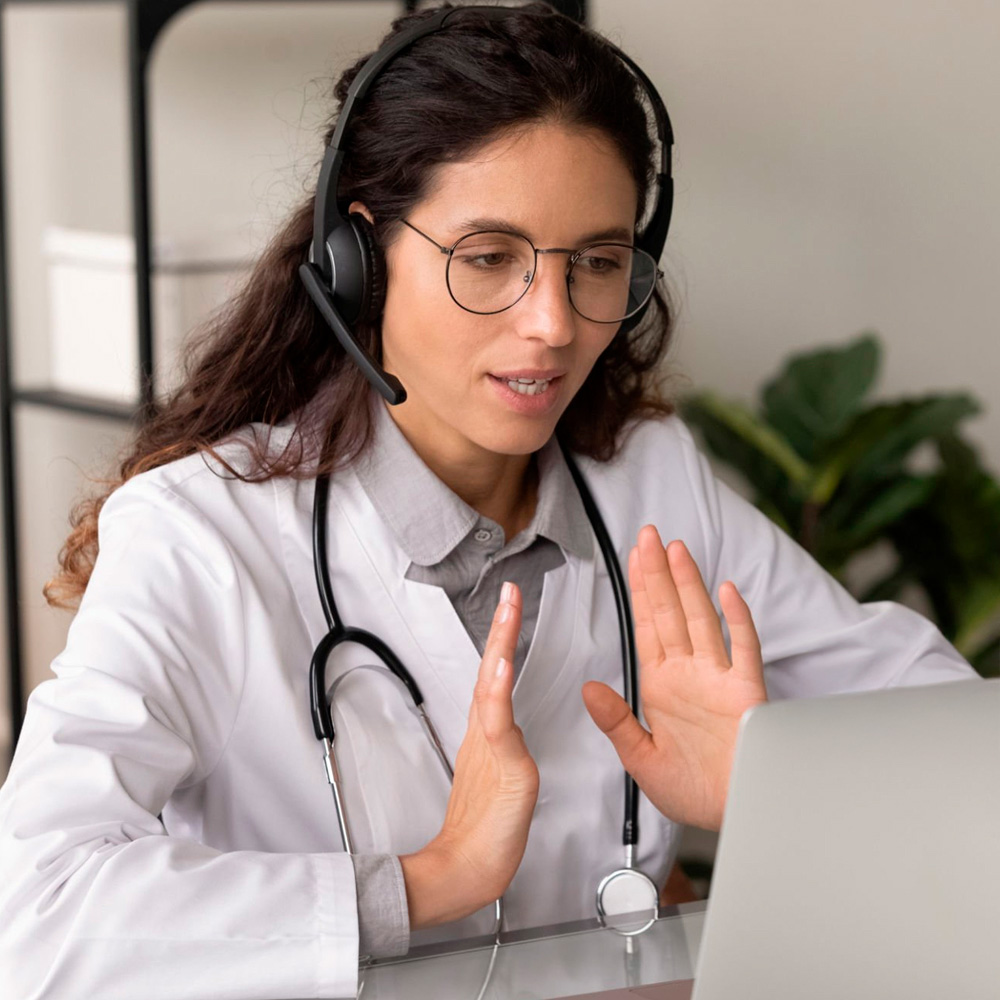 Female doctor with headset and stethoscope conducting an online consultation via laptop.