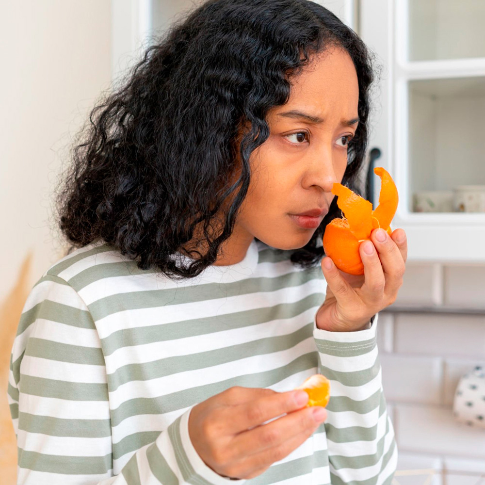 Concerned woman smelling an orange, checking for loss of taste or smell.