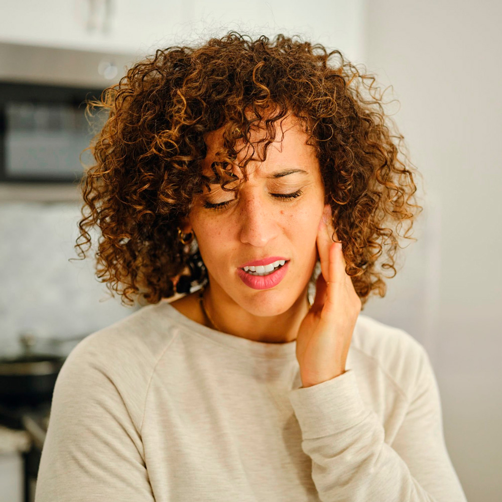 Woman holding her jaw in discomfort, showing signs of TMJ or jaw pain.