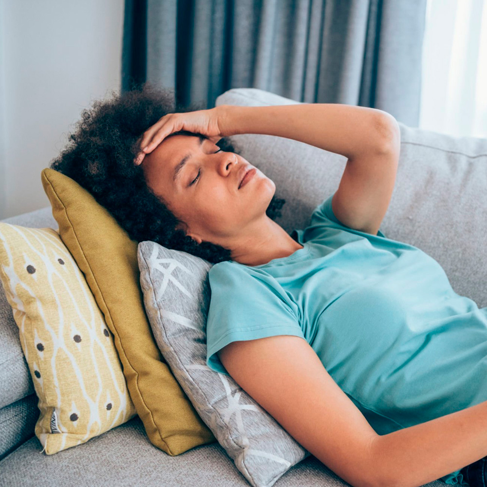Woman lying on couch with hand on forehead, appearing dizzy or unwell.