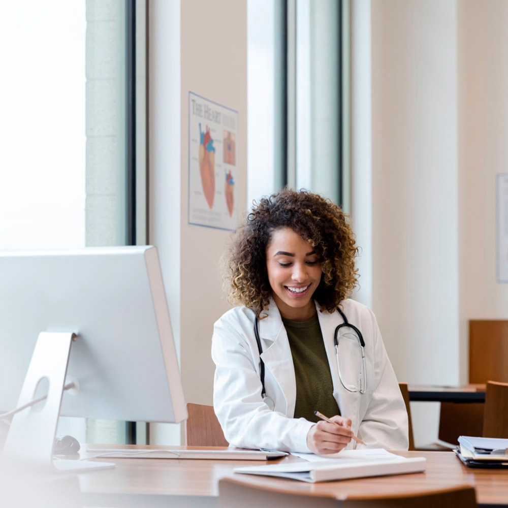 Smiling female doctor writing notes at her desk in a medical office.