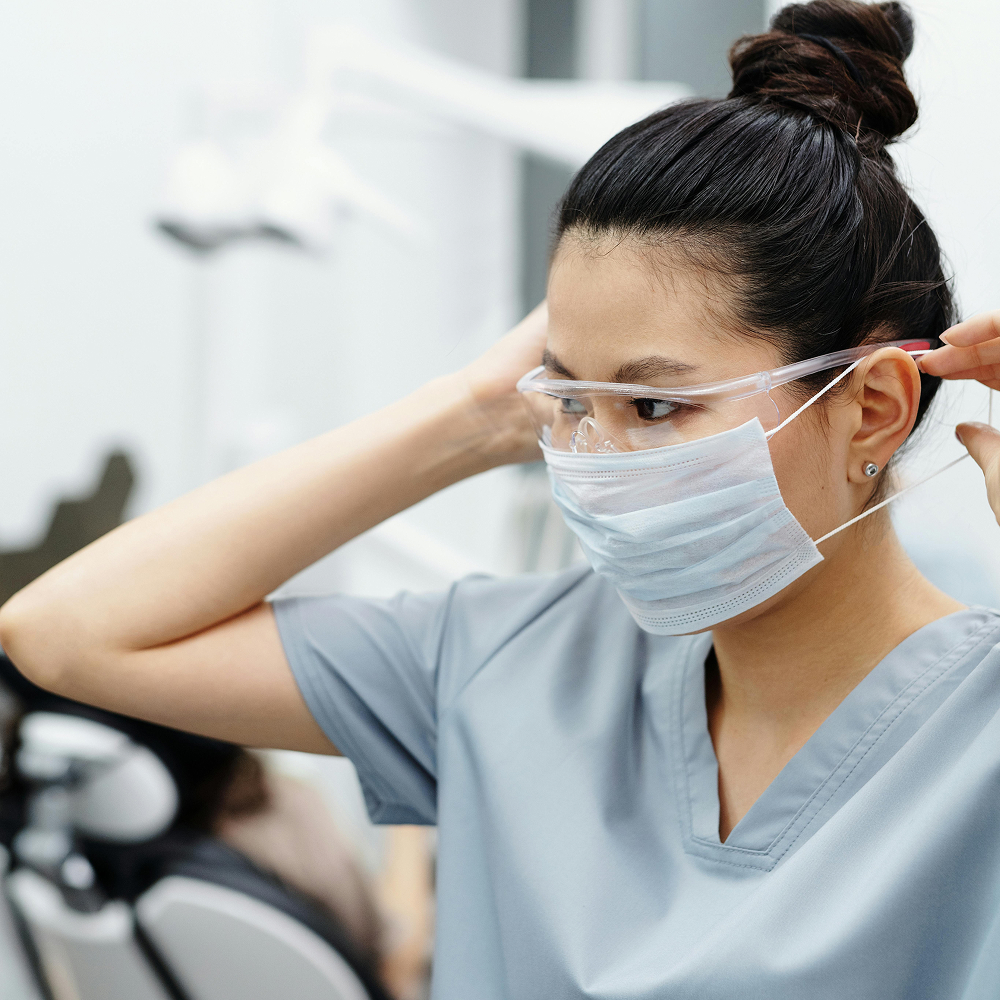 Female dental professional wearing protective mask and goggles in a clinic.