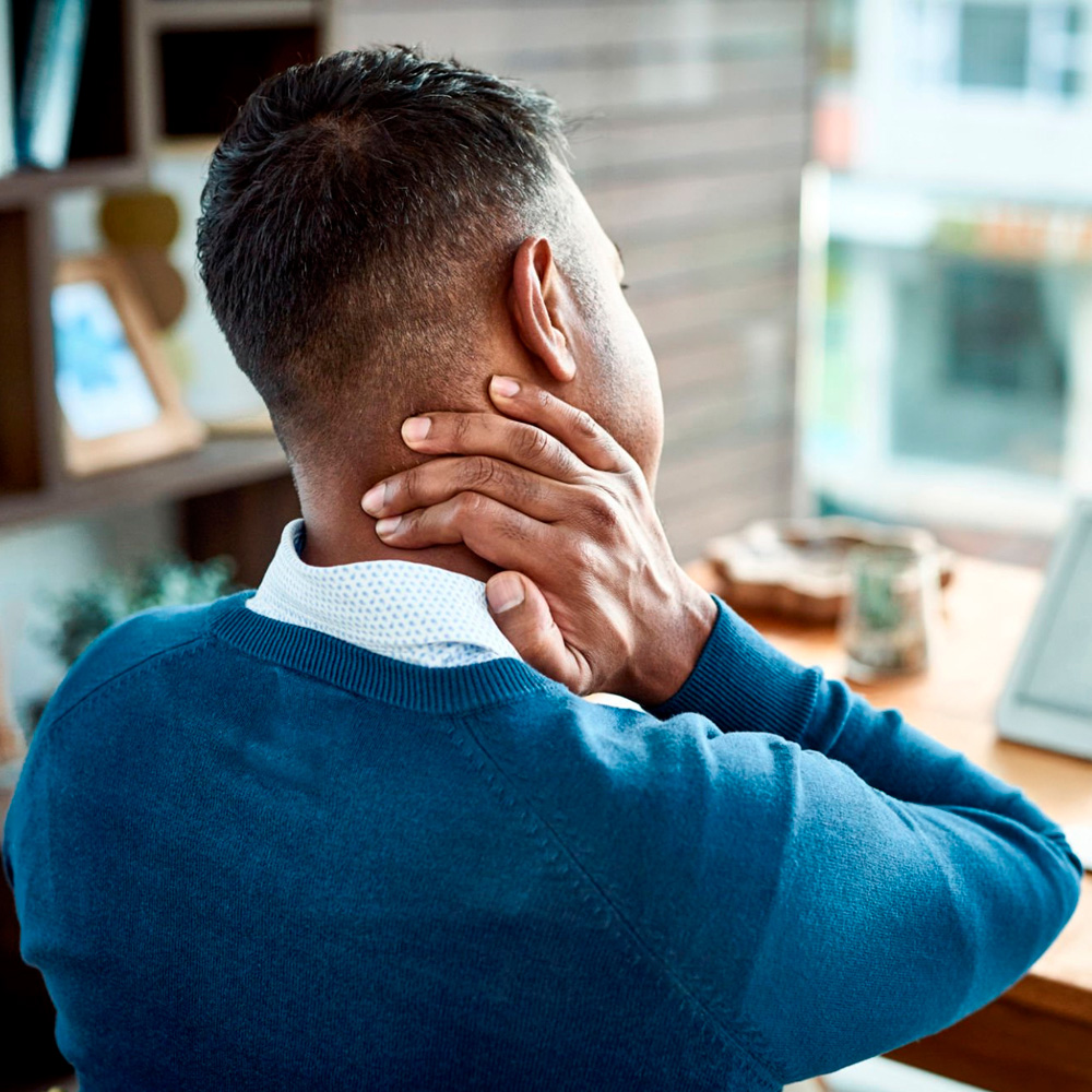 Man holding neck in pain while sitting at desk, seeking relief from neck and back discomfort.