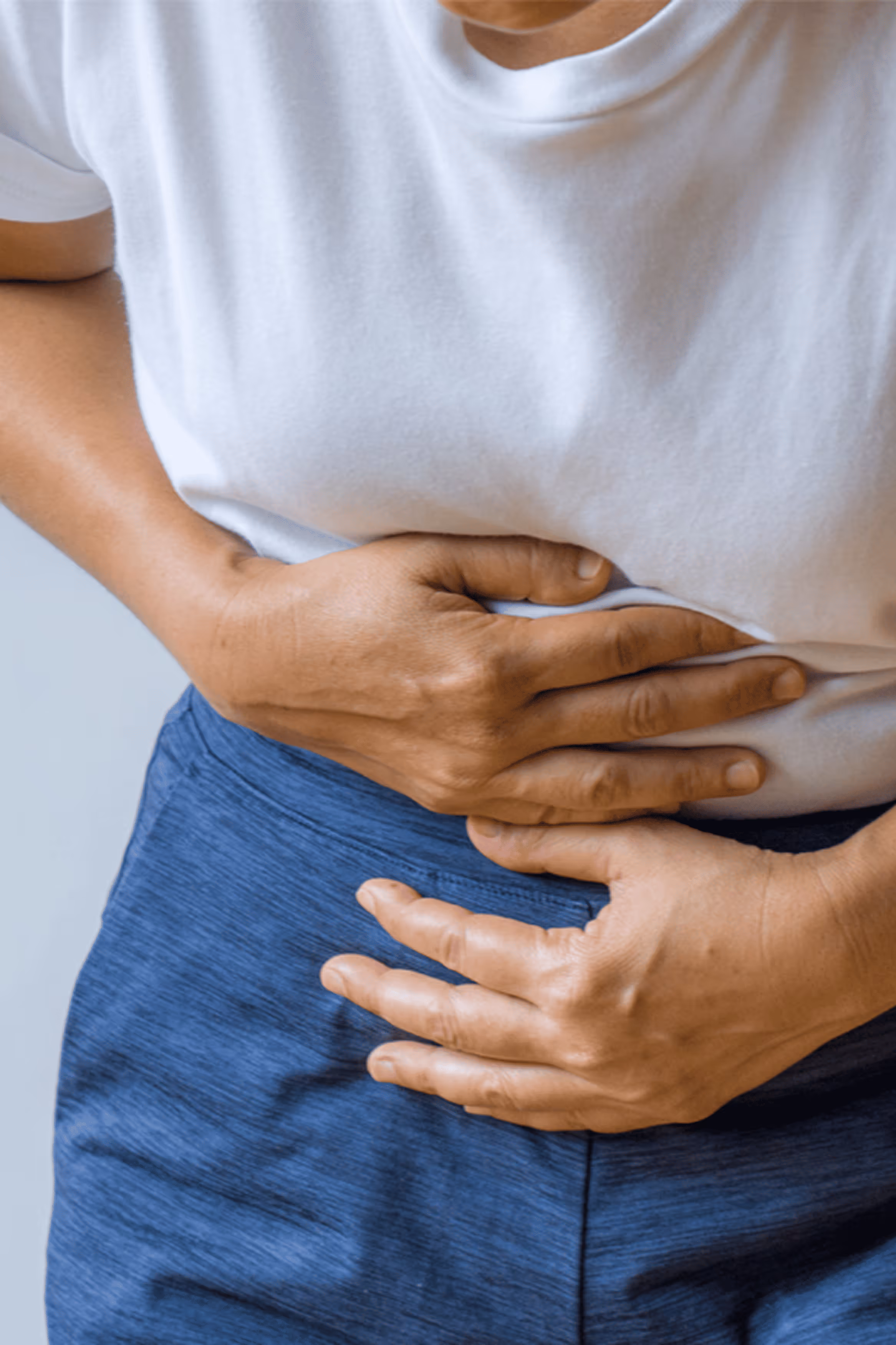 Woman sitting on couch holding her stomach in discomfort.