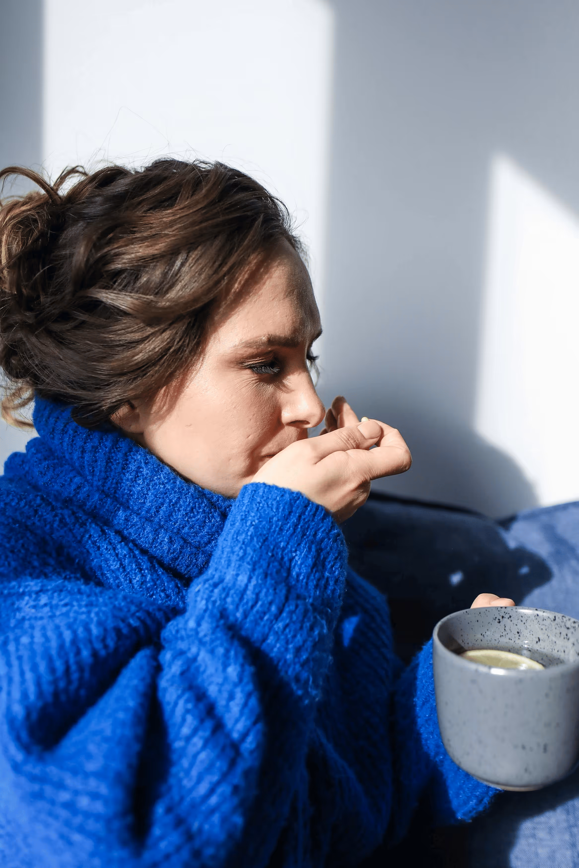 Woman sitting on couch holding her stomach in discomfort.