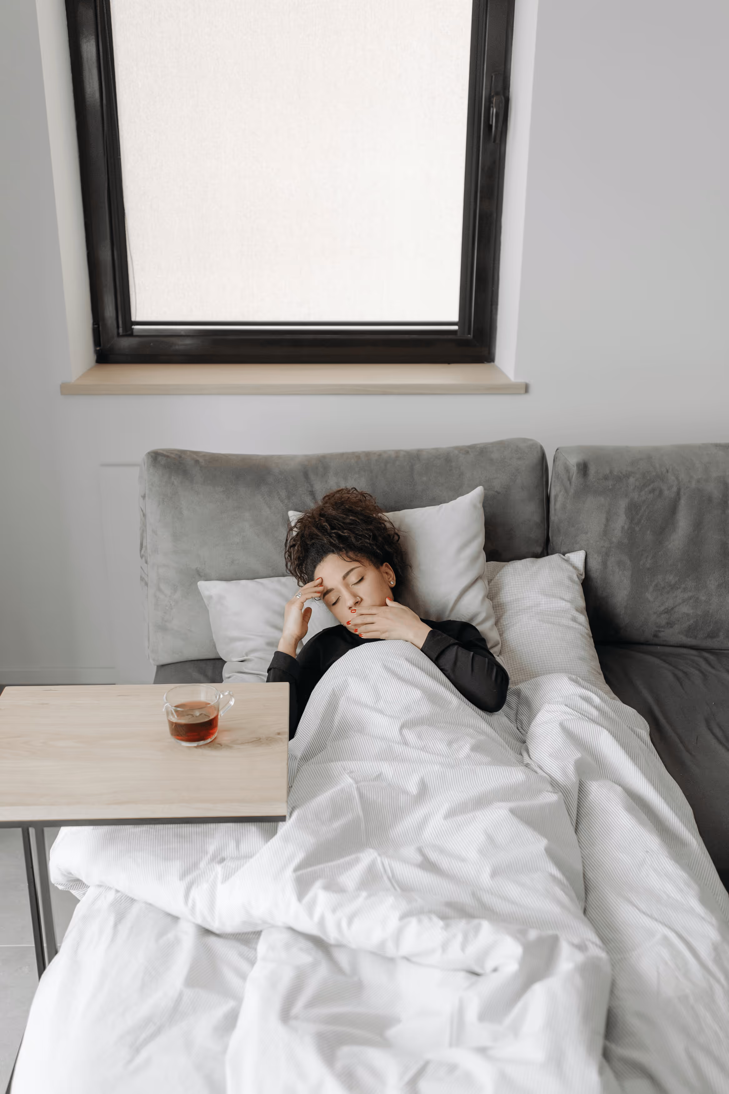 Woman sitting on couch holding her stomach in discomfort.