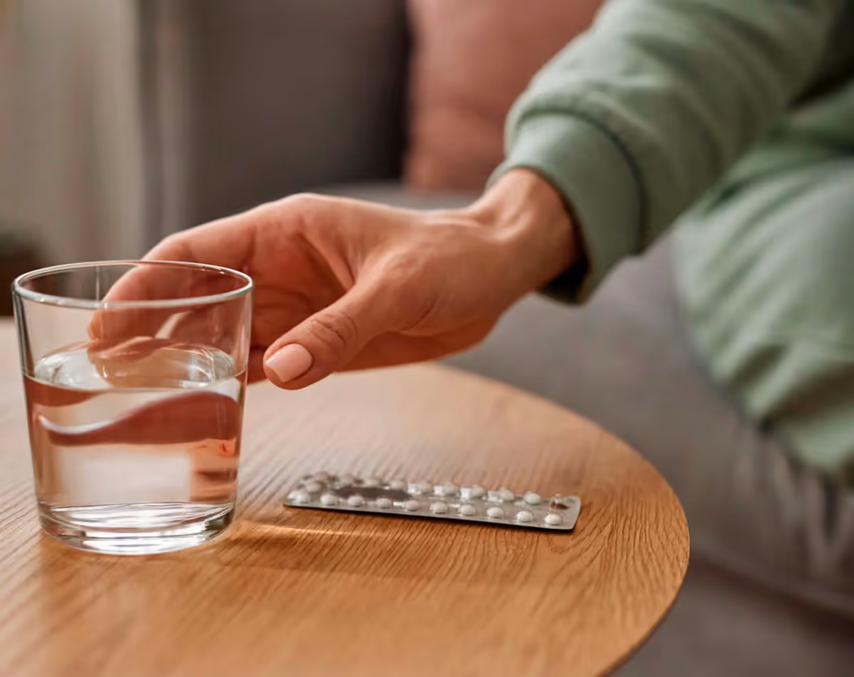 Woman holding glass of water next to birth control tablets.