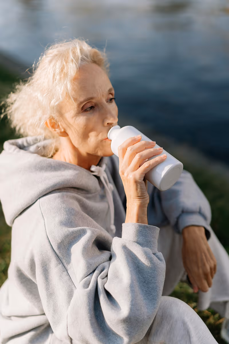 Older woman drinking a shake outdoors as part of Hedfirst metabolic health program.