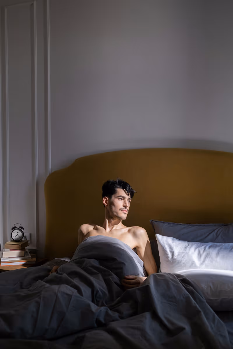 Man sitting in bed, looking thoughtful before treatment for premature ejaculation.