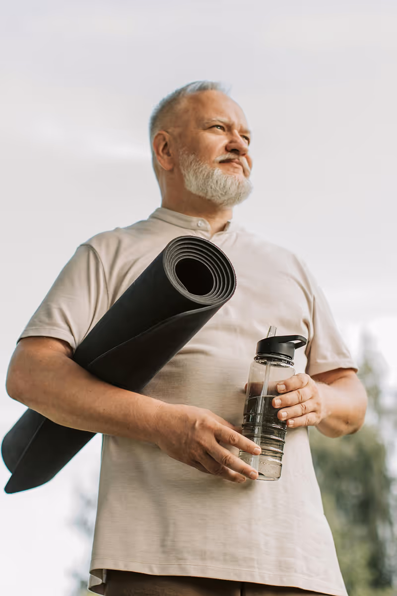 Man holding yoga mat and water bottle, promoting Hedfirst metabolic health treatments for energy balance and vitality.