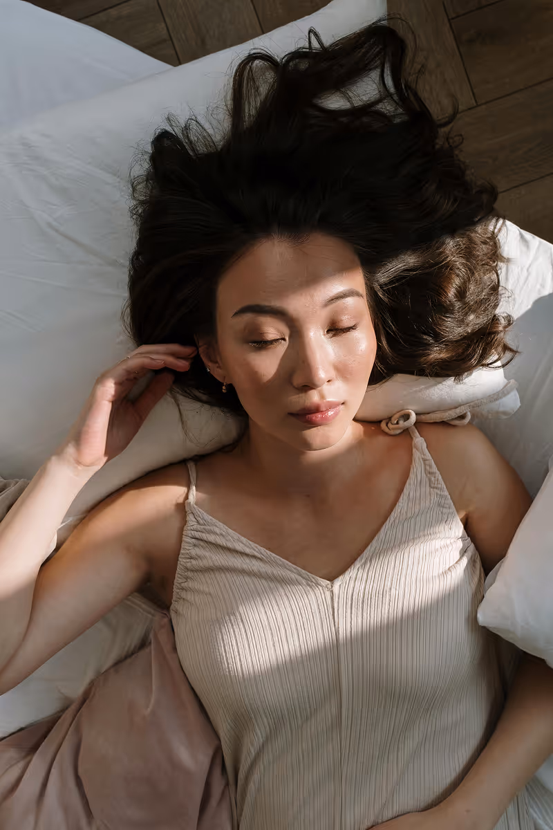Woman lying on bed in soft beige clothing, representing fertility care and balance.