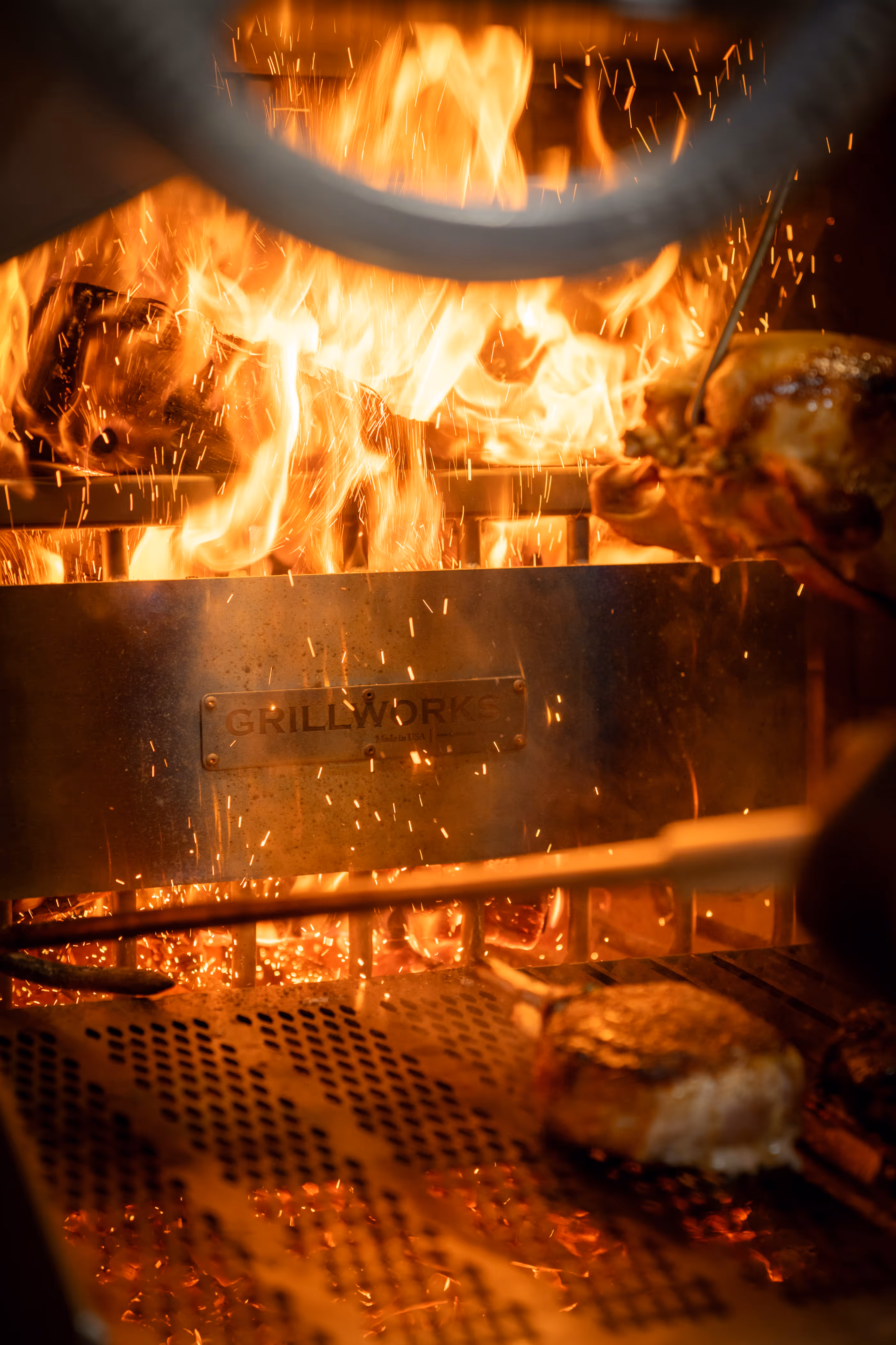 Close-up of a sizzling grill with intense flames, vibrant sparks, and a juicy piece of meat roasting, conveying a sense of heat and flavor.