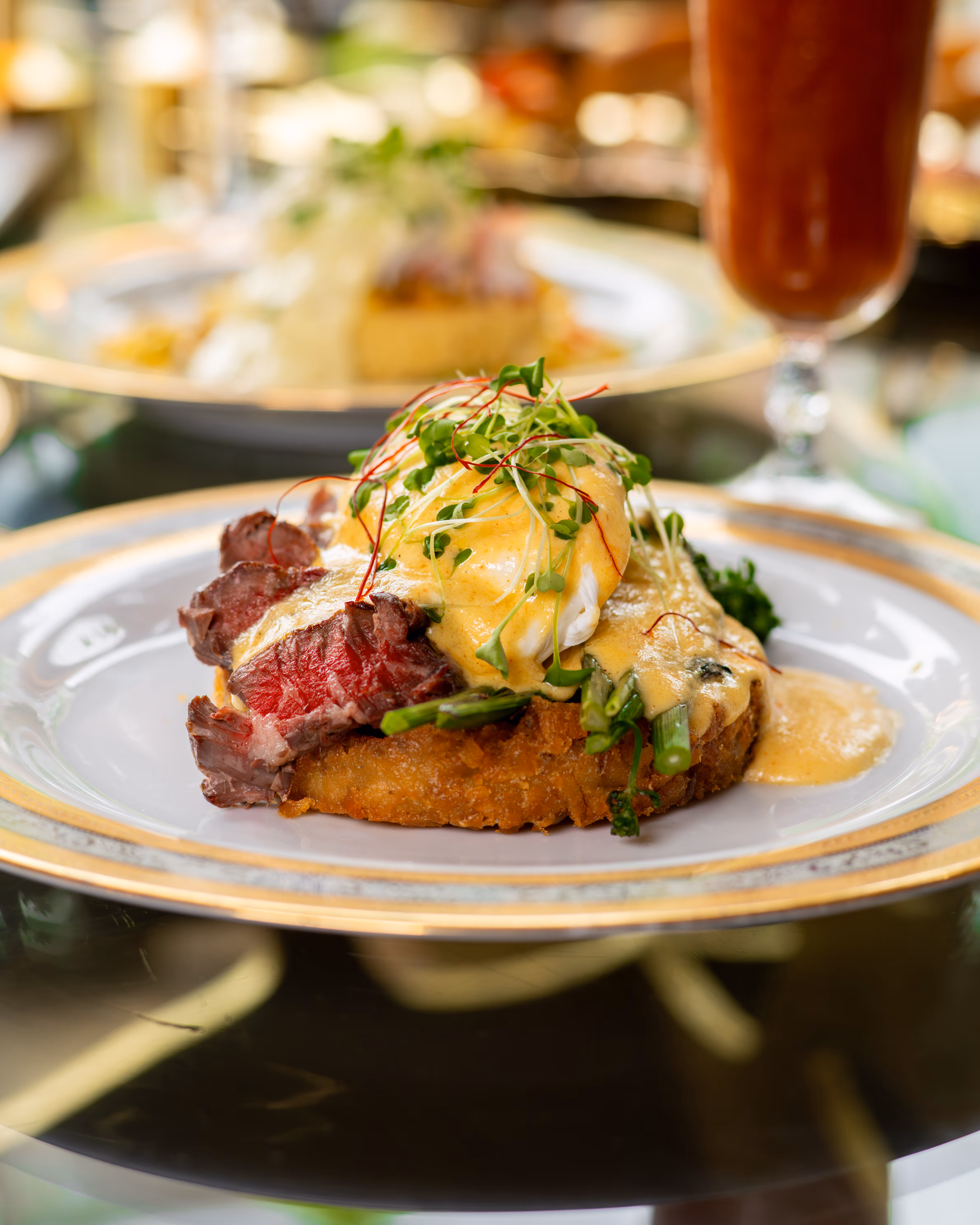 Plate with steak, poached egg topped with hollandaise sauce and microgreens on a crispy base.