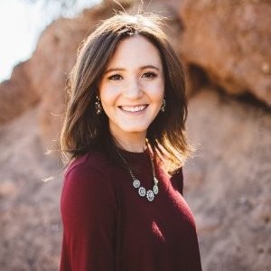 Smiling woman with shoulder-length brown hair wearing a maroon top and silver necklace outdoors.