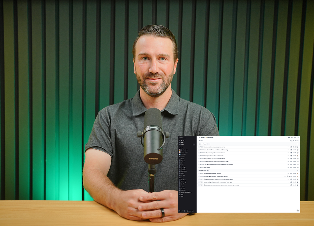 Man with a beard and short hair sitting at wooden desk with hands clasped, speaking into a microphone, with a digital task list overlay on the right.