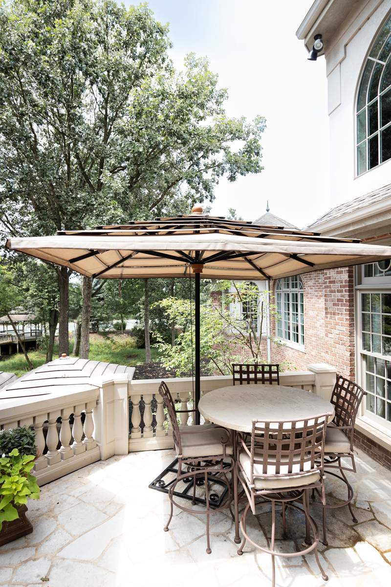 A round patio table with six chairs sits under a large umbrella on a stone terrace.