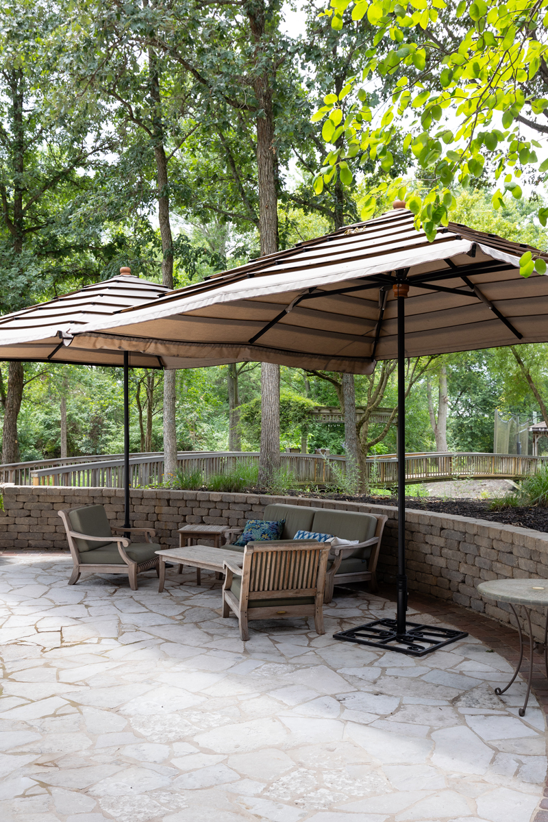 A patio with wooden seating and a large, striped canopy surrounded by trees.