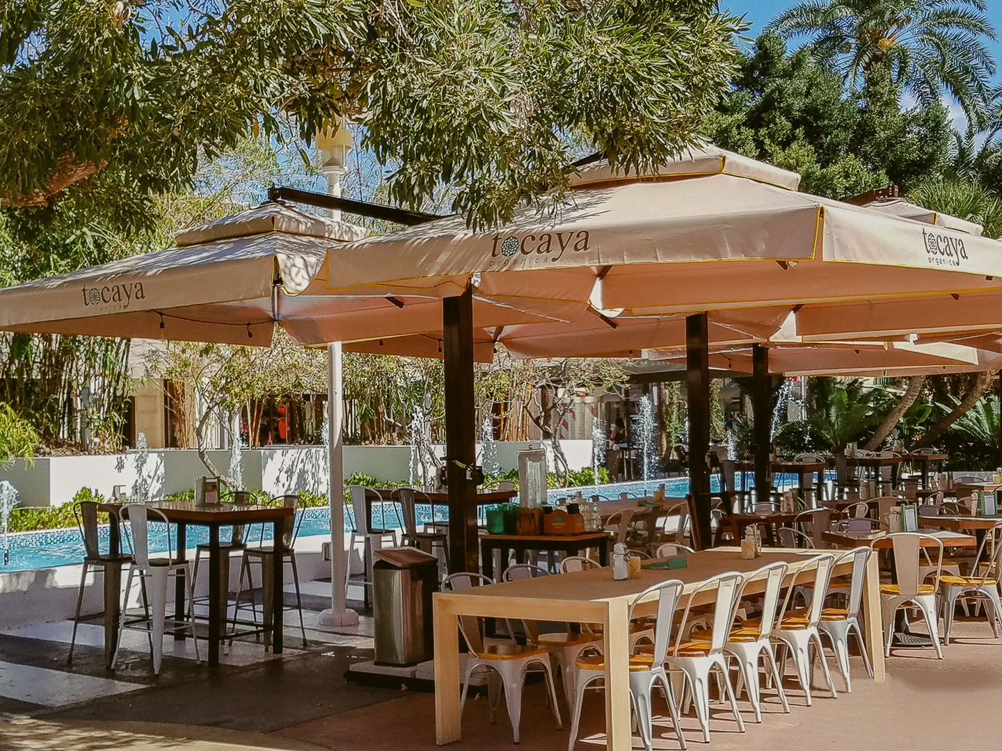 Outdoor restaurant with tables and chairs under large umbrellas near a pool.