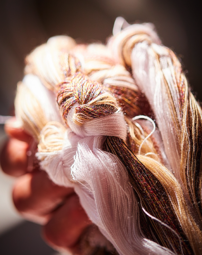 A hand holding bundles of multicolored yarn threads under bright light.