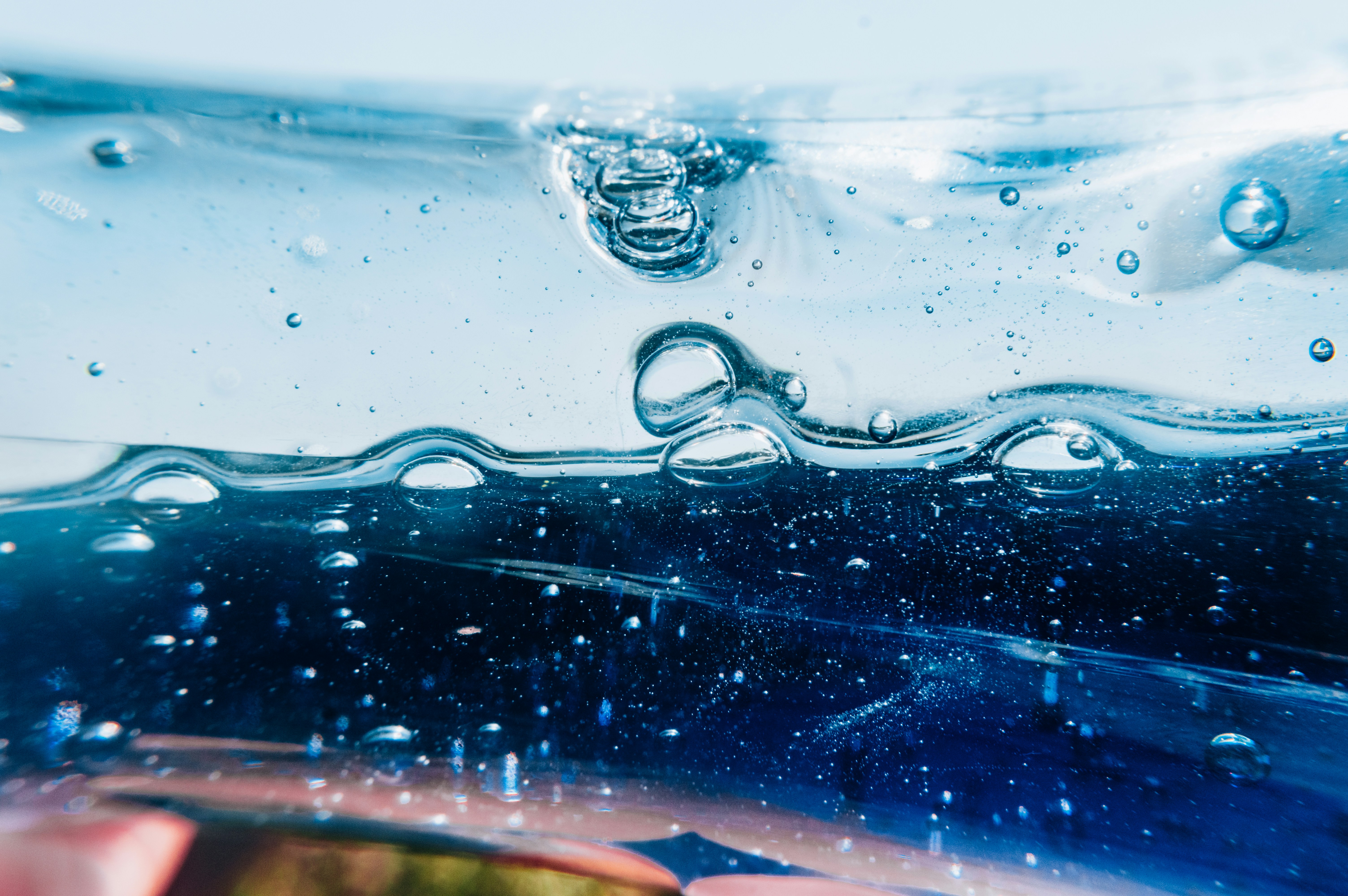 Close-up of bubbles rising through clear, blue-tinted liquid, creating a wavy pattern.