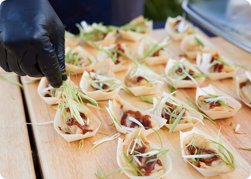 Hand wearing a black glove garnishing small dishes with fresh green herbs on a wooden table.