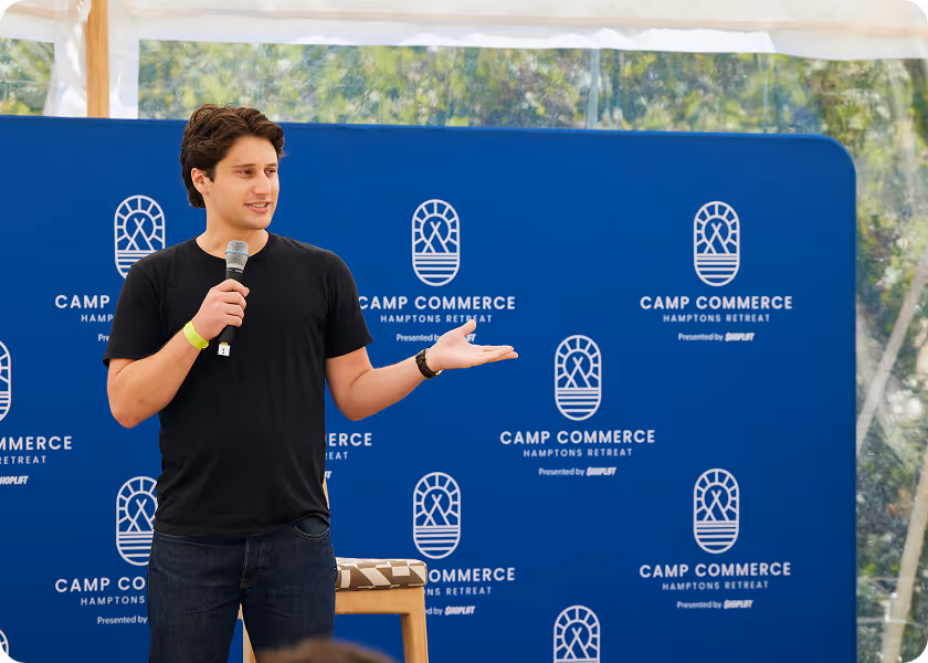 Man in black shirt holding a microphone speaking at Camp Commerce Hamptons Retreat event.