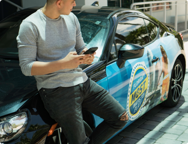 Person leaning on car with branded wrap, checking smartphone