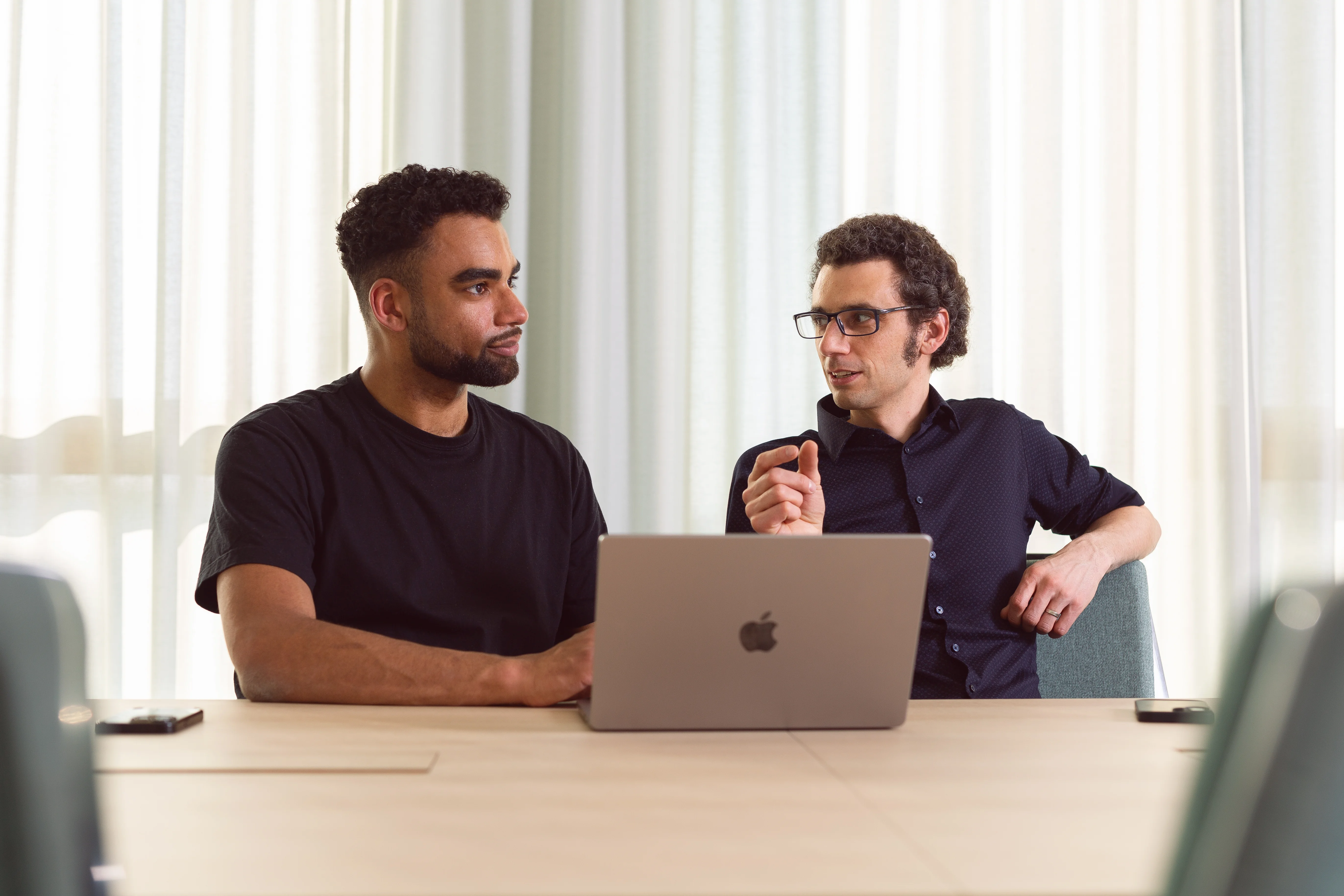 Zwei Männer besprechen etwas und sitzen dabei vor einem Laptop