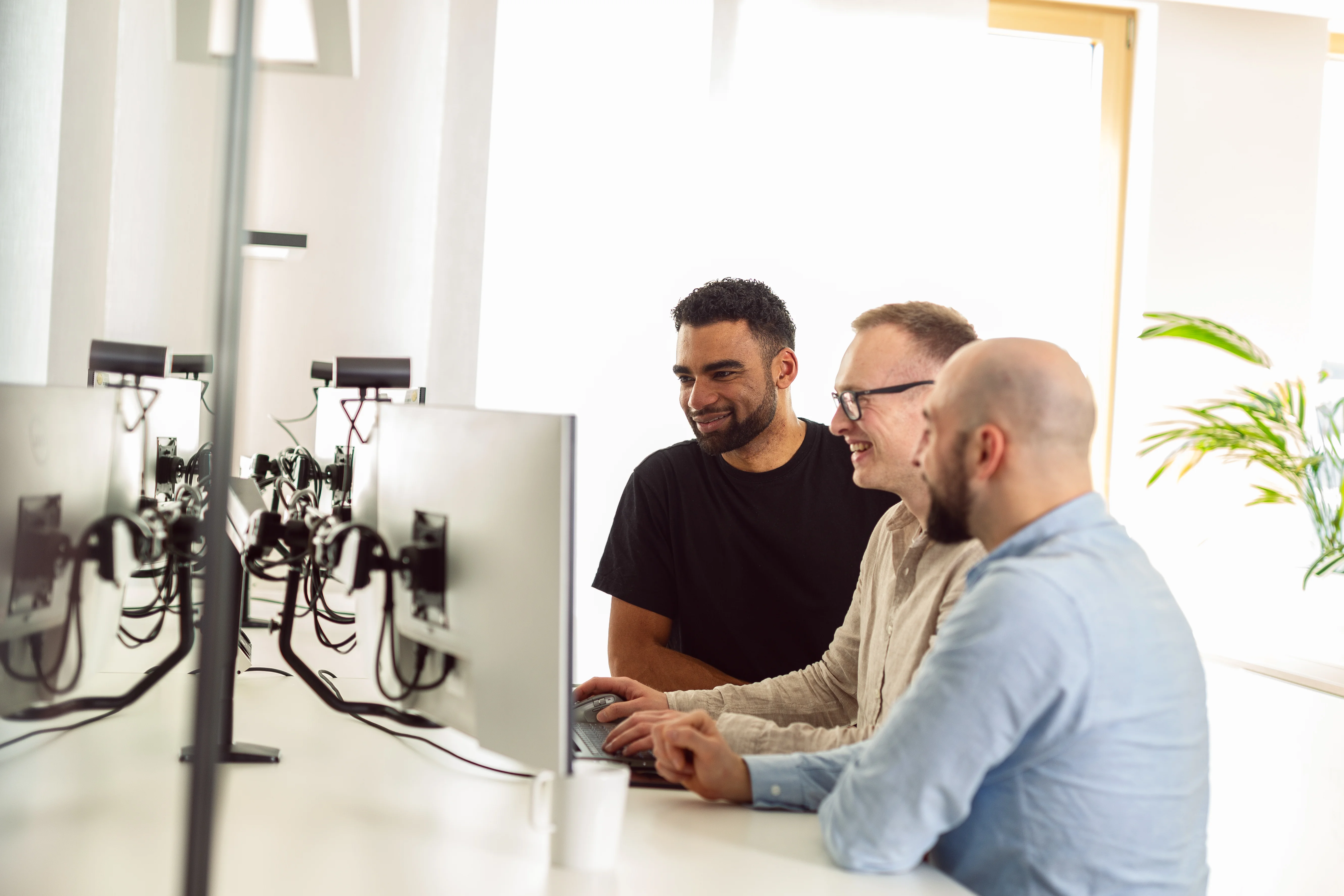 Drei Männer stehen an einem PC-Arbeitsplatz und besprechen am Monitor