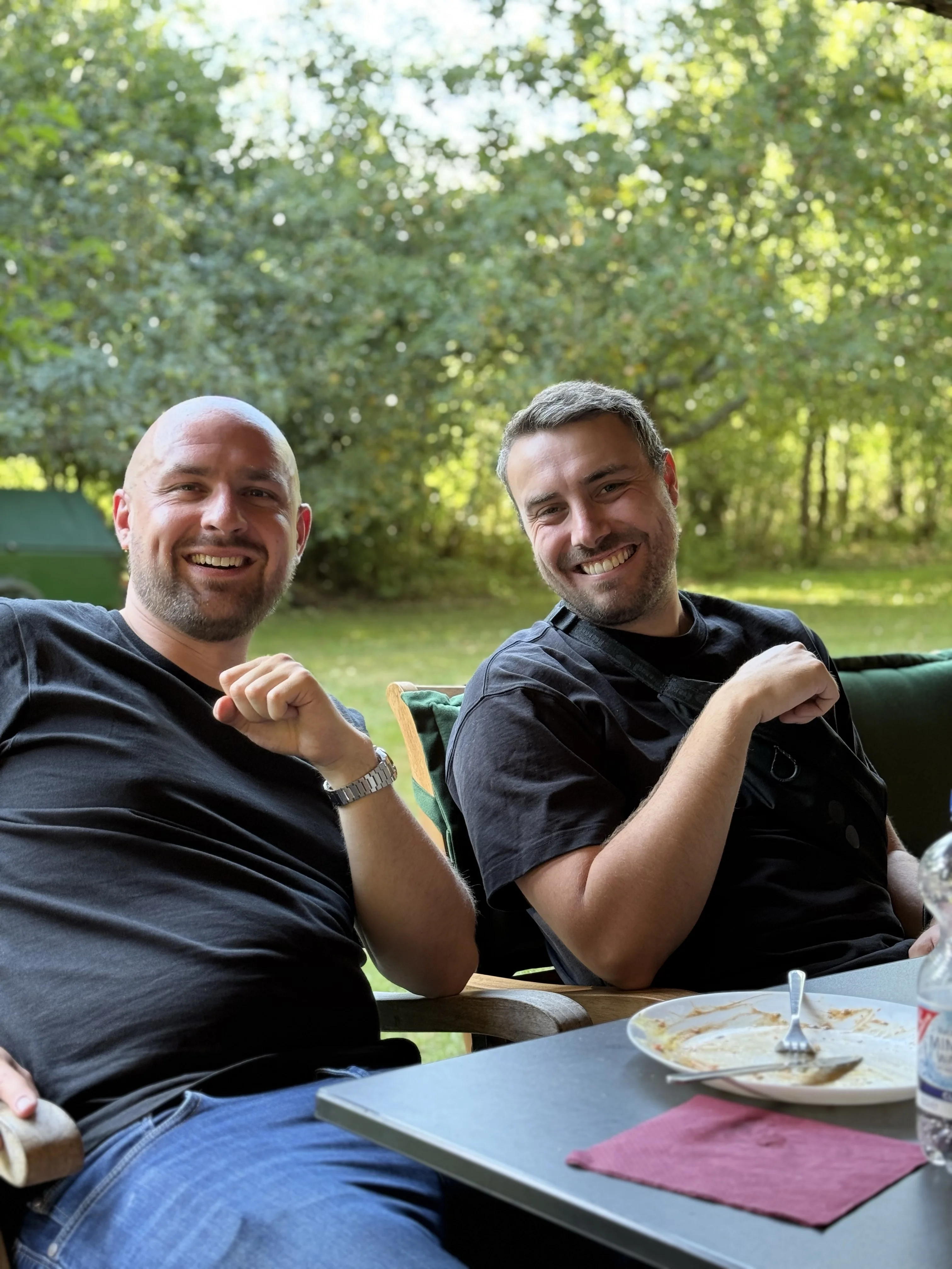 Zwei gut gelaunte Leute am Tisch sitzend in einem Garten