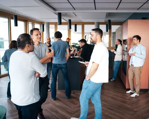 EIne Gruppe von Leuten vor und an einer Stehtheke in einer Lounge bei Gesprächen und Pizza