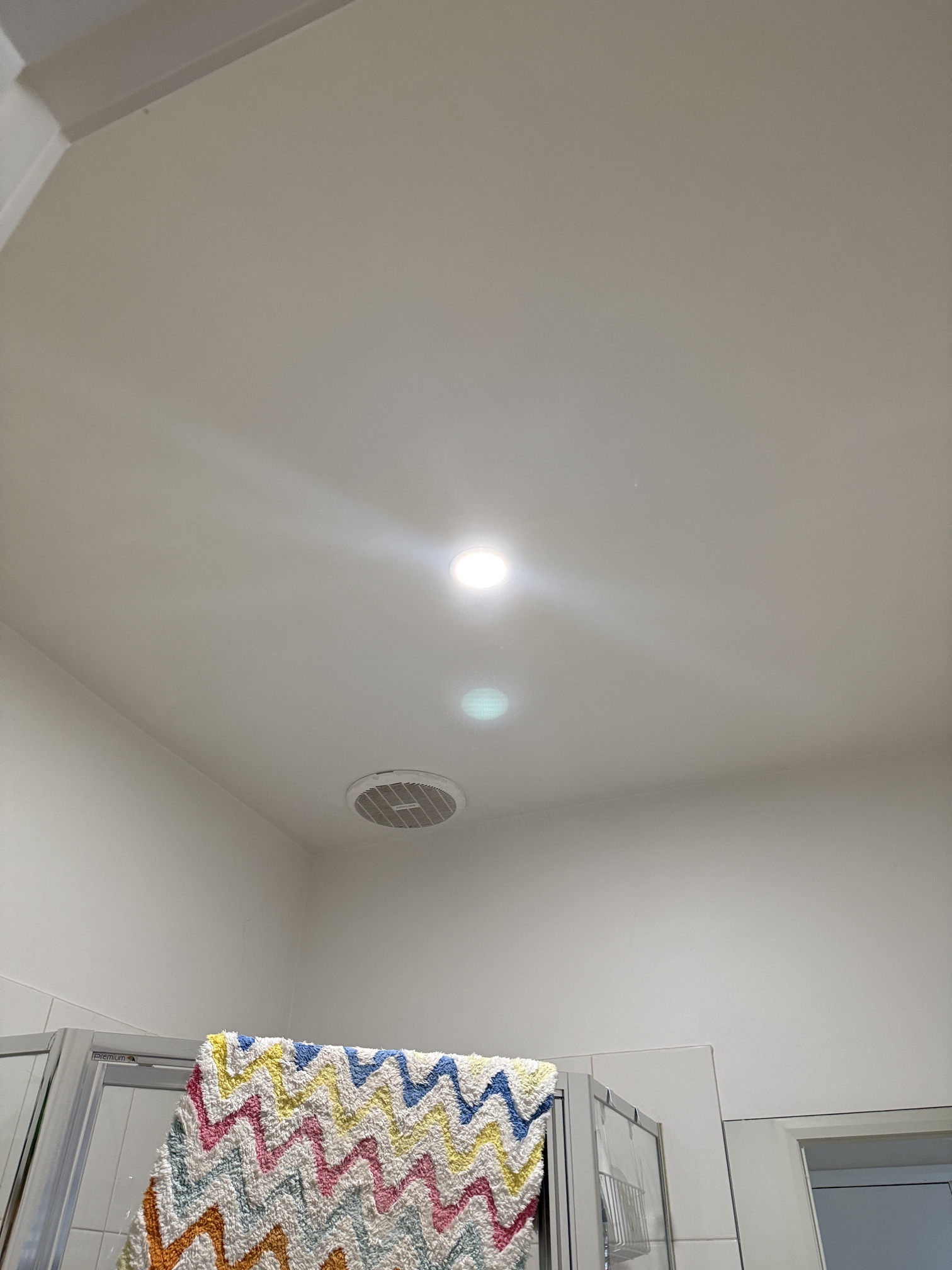 Modern LED downlight shining in a bathroom ceiling next to an older exhaust grille