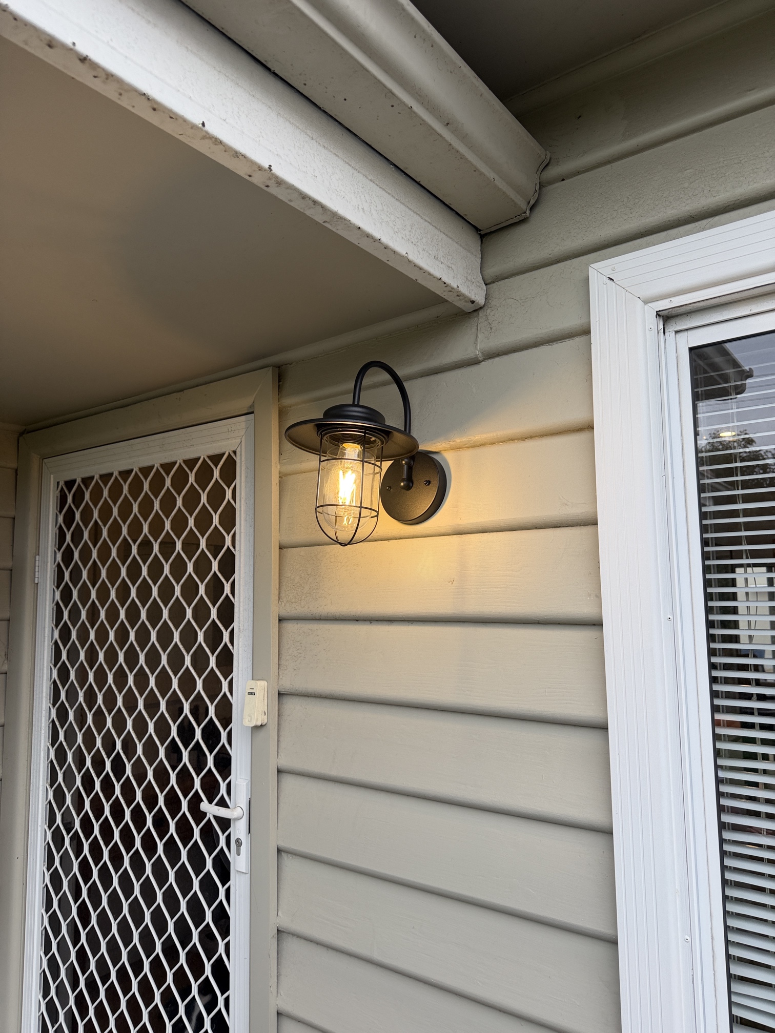 Modern black exterior wall light installed beside the front door of a Carrum home by Ferguson Electrical with warm LED lighting creating a welcoming entrance.