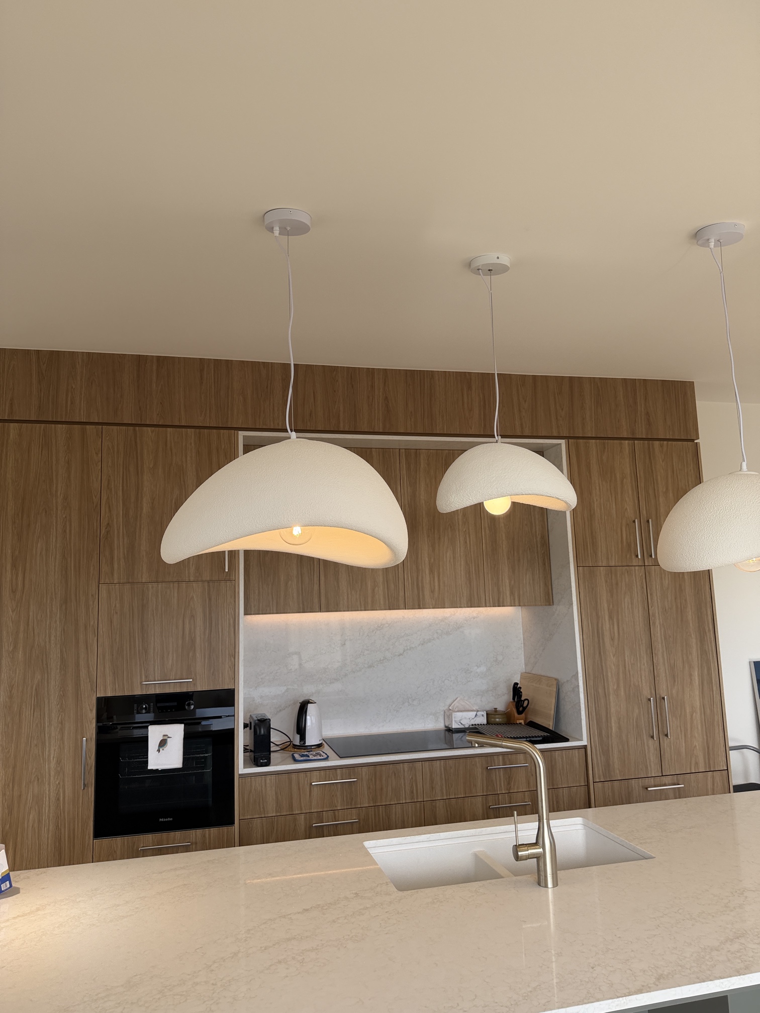 Three modern white pendant lights installed above a kitchen island in a newly built Black Chalk Homes residence in Rye by Ferguson Electrical.