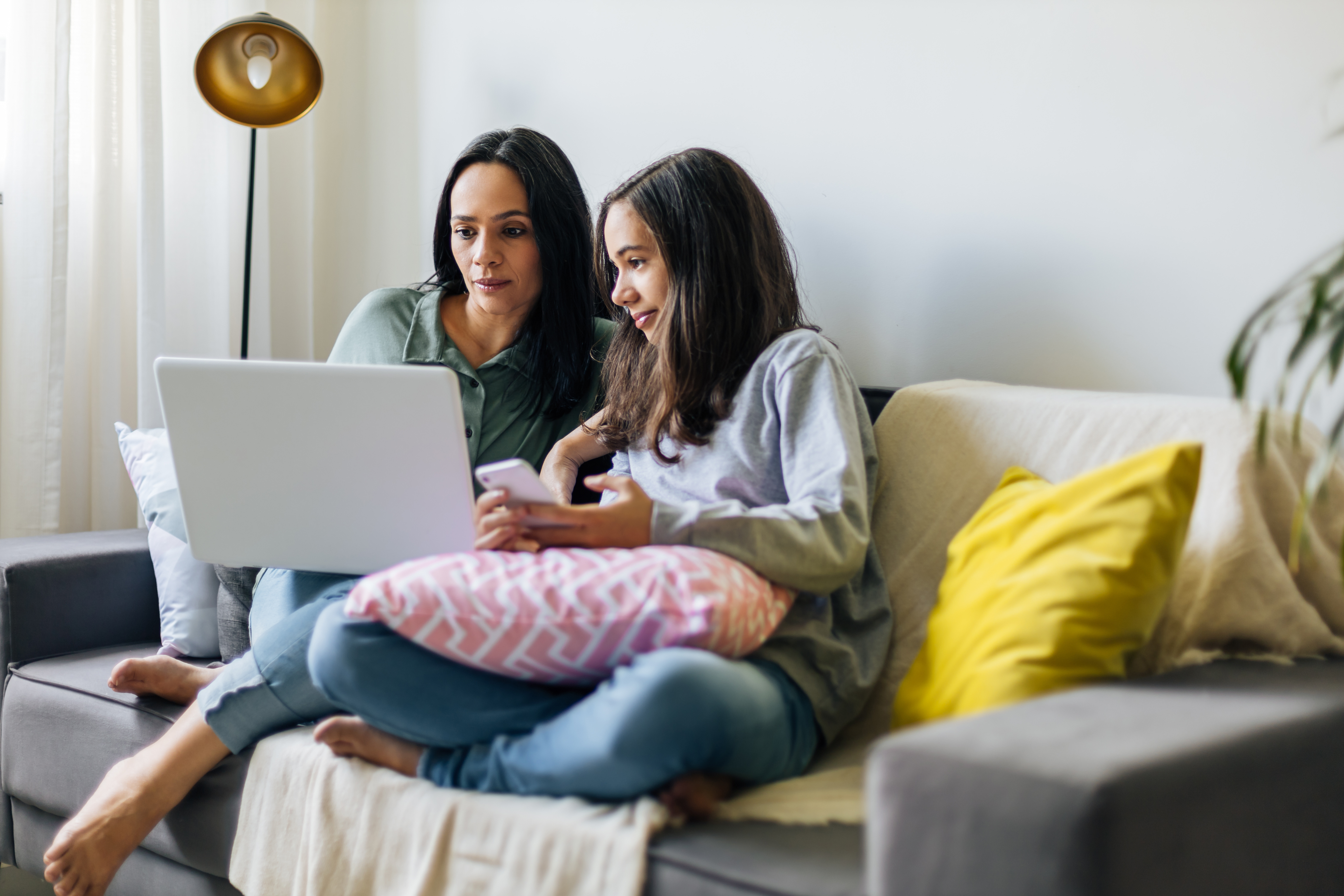 A parent and child sitting on a white couch looking at a laptop computer.