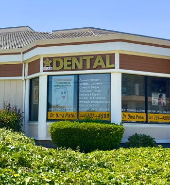 Exterior view of a dental clinic with signage for Dr. Uma Patel and services listed, surrounded by greenery.